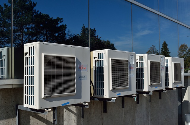 The image shows several air conditioning units mounted on an exterior wall. Each unit is white with a grid-like front, and they are installed above a smooth concrete base, reflecting the surrounding environment.